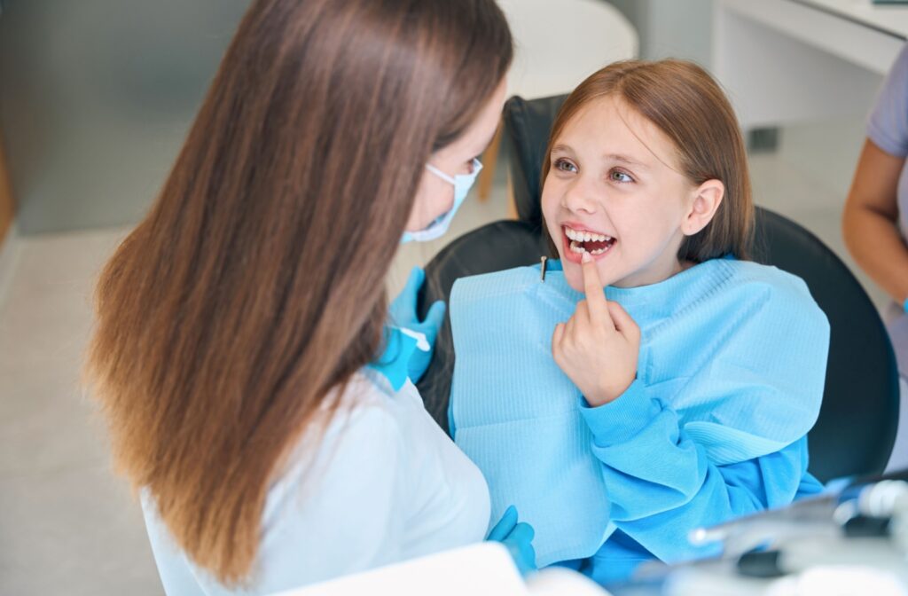 Young girl smiling and pointing to her teeth during a dental examination with a pediatric dentist at London Little Bites Dentistry, wearing a blue dental bib in a clean, modern dental office.