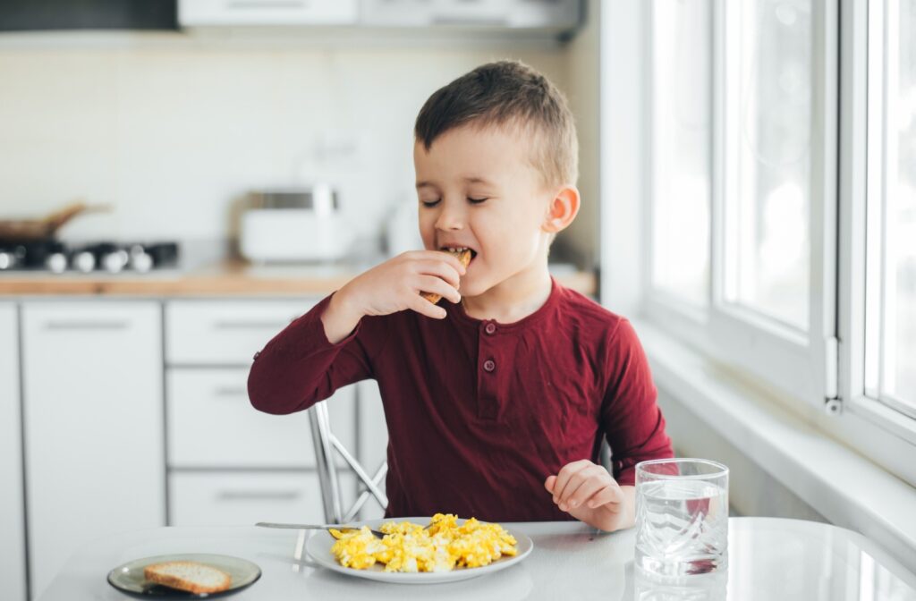 A child sitting infront of a plate full of scrambled eggs.